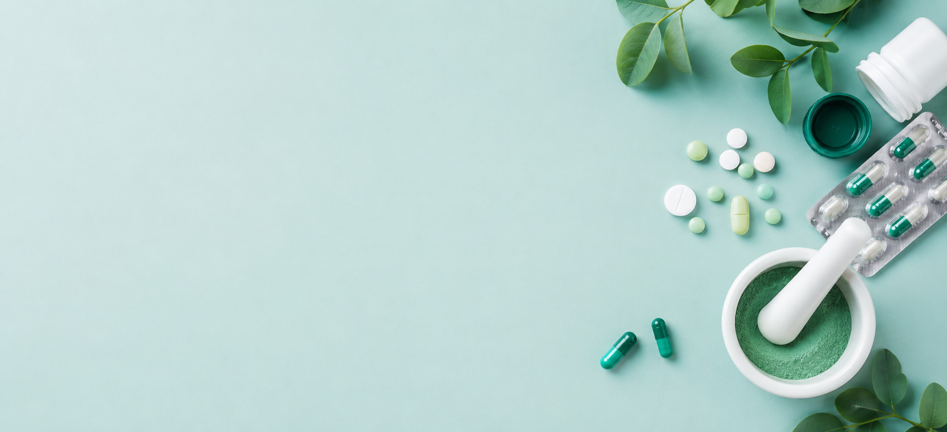 Herbal capsules, tablets and a mortar of green powder on a mint background